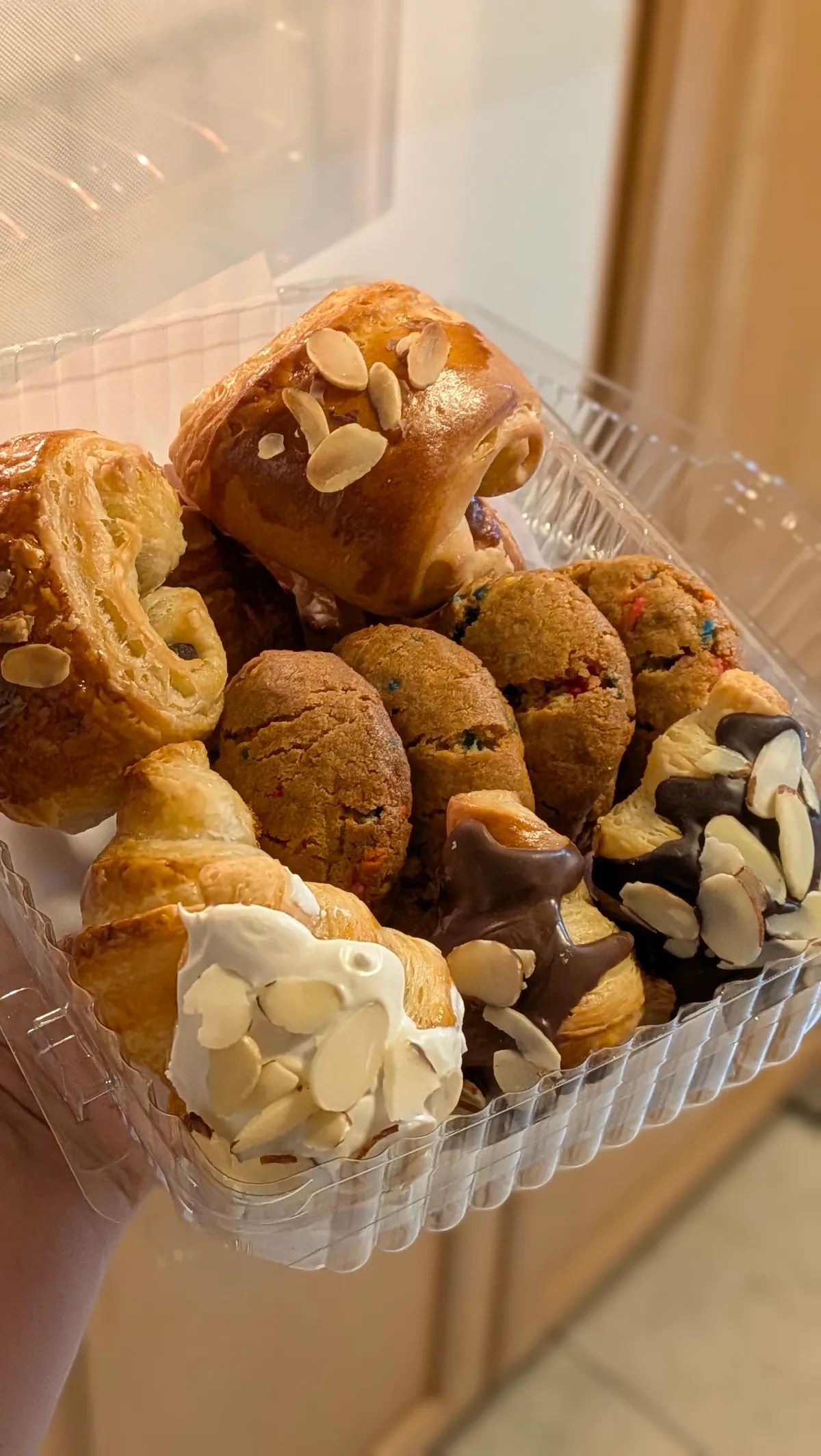 Caja transparente con doce piezas mini surtidas: croissants cubiertos de chocolate y almendra, chocolatines y galletas